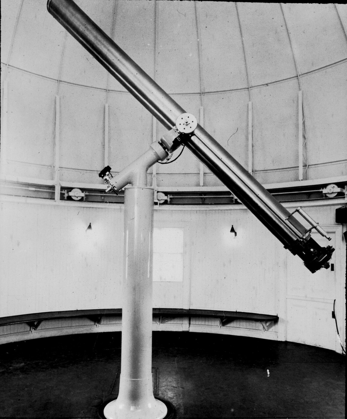 A vintage photograph of a large camera assembly on a telescope mount with a man standing beside it in a domed observatory.