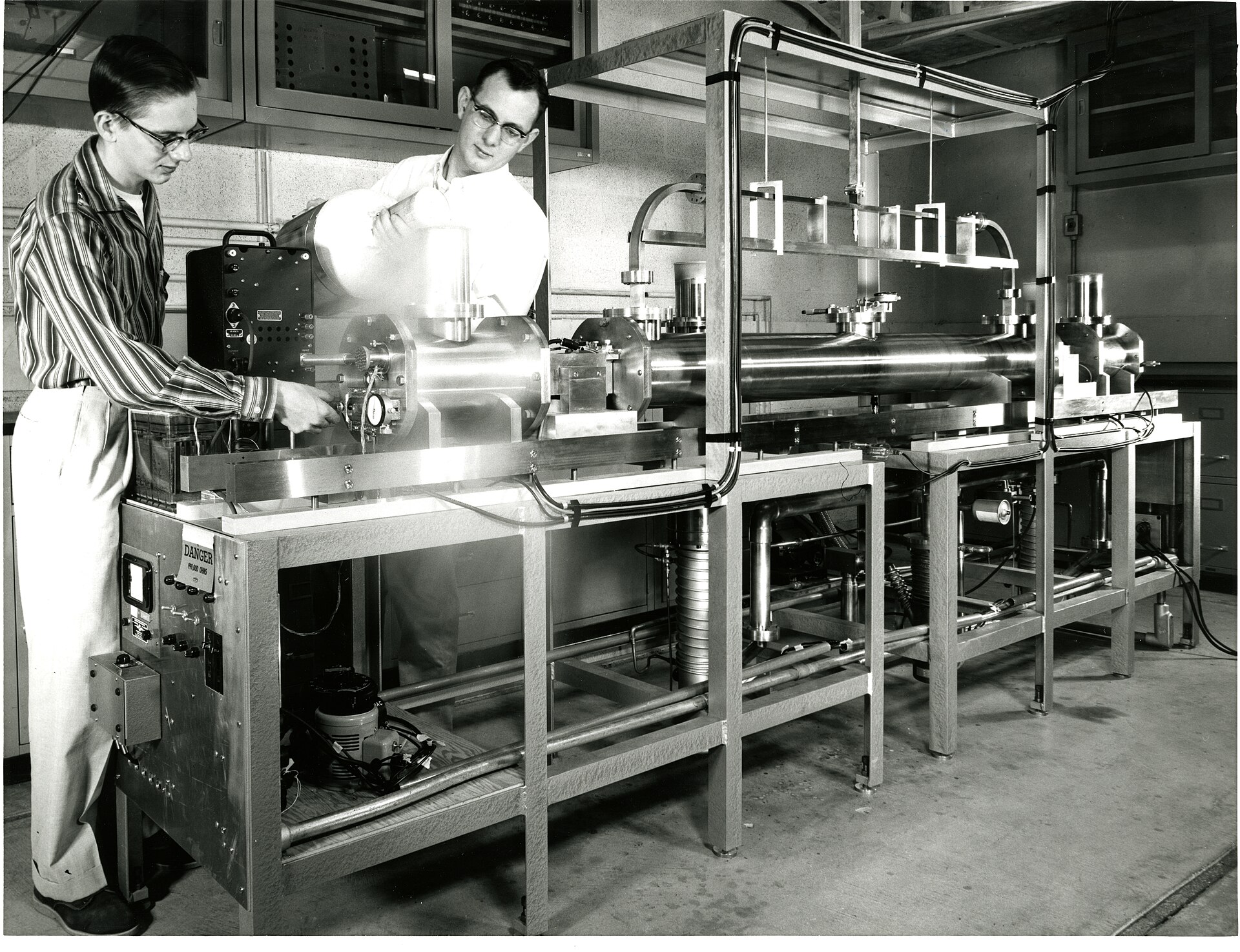 Two scientists at the US National Bureau of Standards in the 1950s working on an early caesium beam atomic clock, one pouring liquid nitrogen over a cold trap.